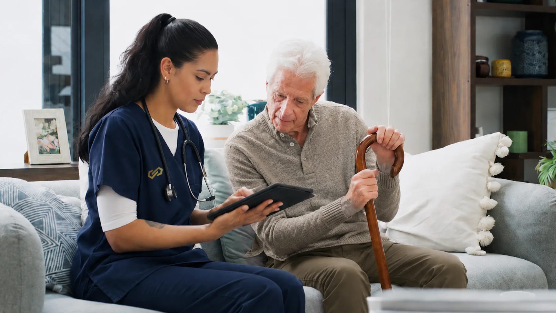 A nurse goes through notes on a tablet with an older man holding his cane