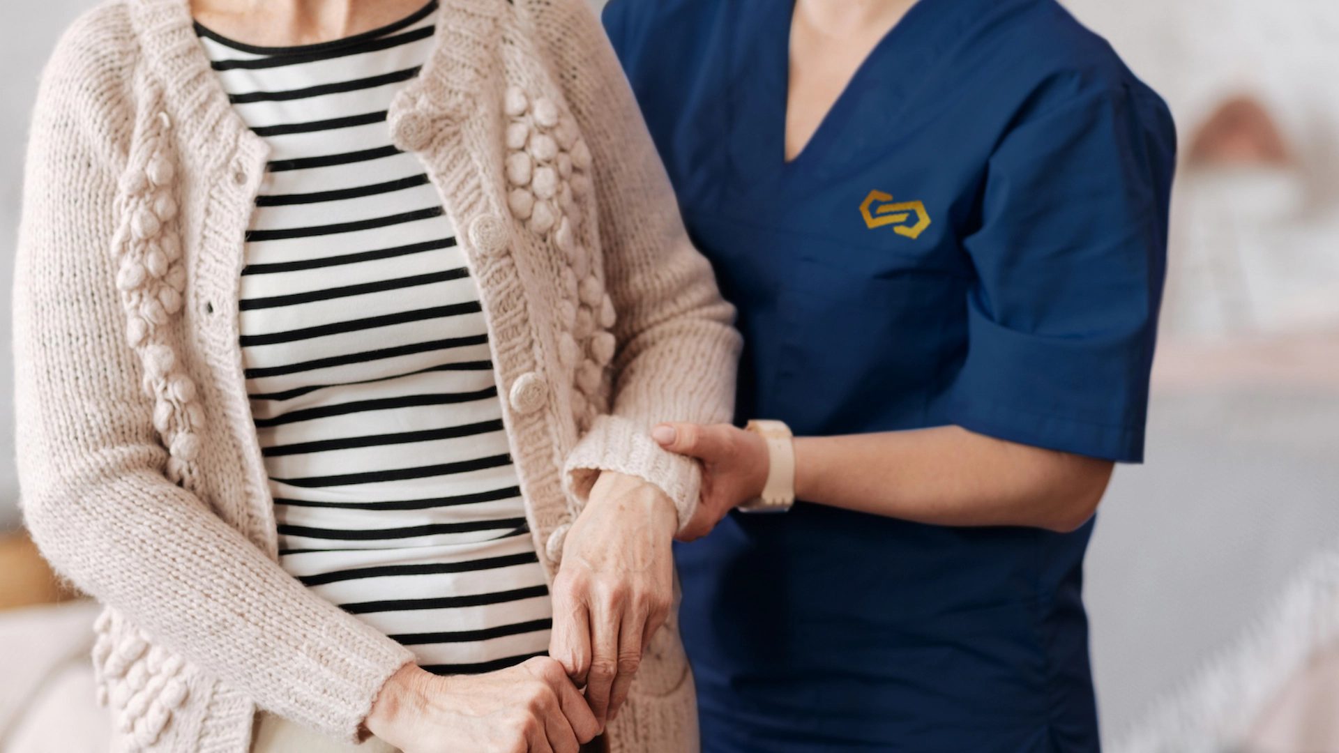 A nurse steadies an older woman's arm as she rises to her feet