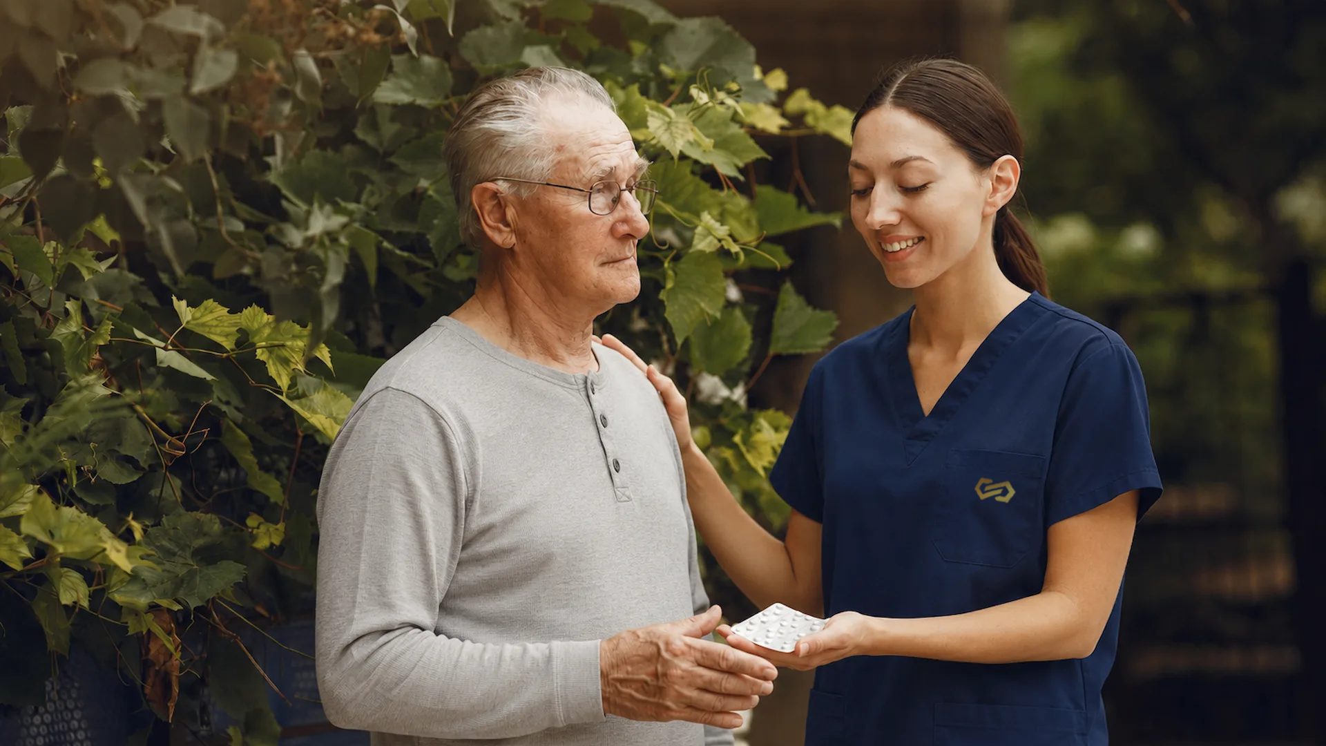 A nurse hands a pack of medication to an older man in the garden