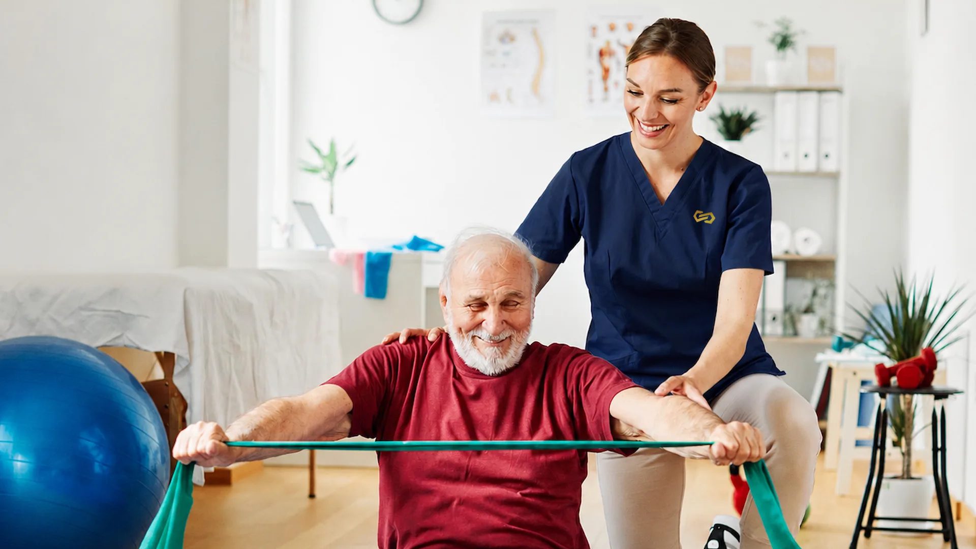 A therapist guides an older man through a seated resistance band exercise
