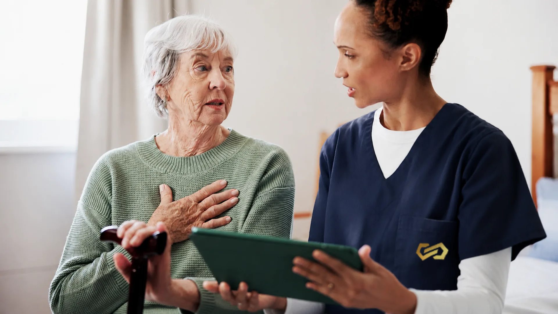 A nurse shows a tablet to an older woman with a cane as the two talk