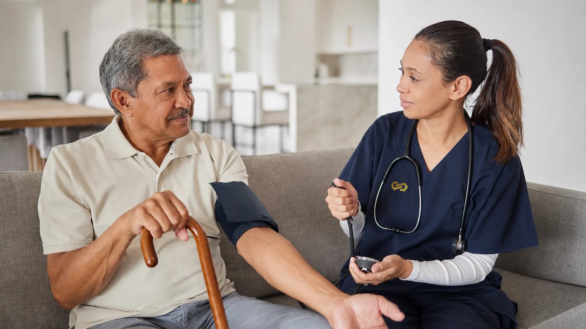 A nurse takes an older man's blood pressure while he rests on the sofa